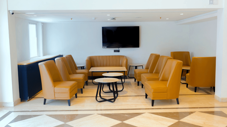 A lounge area at Pride Premier Greater Noida featuring several cushioned armchairs and small round tables on a marble floor.