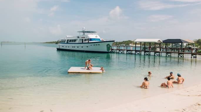 Shoreline with dock, anchored boat, people in swimwear in shallow water, Abaco Inn.