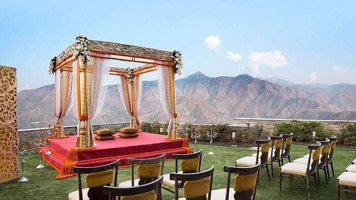 a mandap set up meant for wedding ceremony on manicured lawn with chairs facing it and in the background there are hils at a distance- neer ganga Resorts