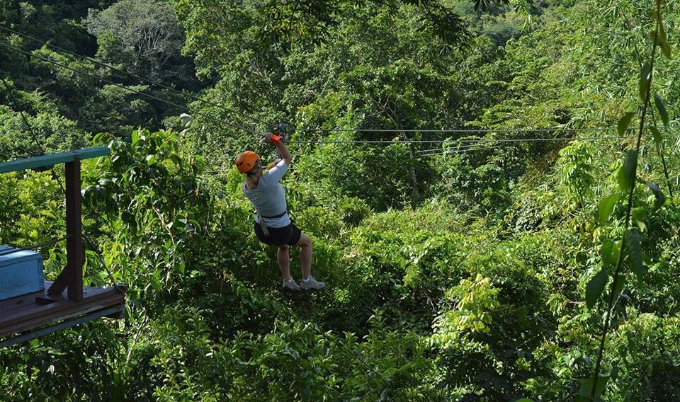  A person wearing a harness and helmet is seen ziplining through a lush green jungle on a sunny day - Tamarind Hills Resort and Villas - Antigua