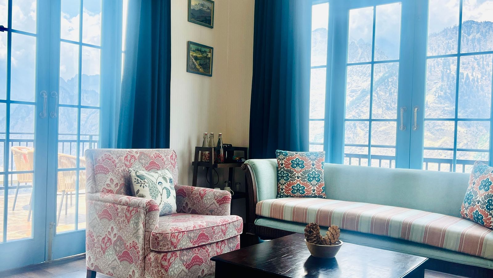 Hotel lounge with pink sofas, blue curtains, and large windows with views | Faraway Cottages, Auli
