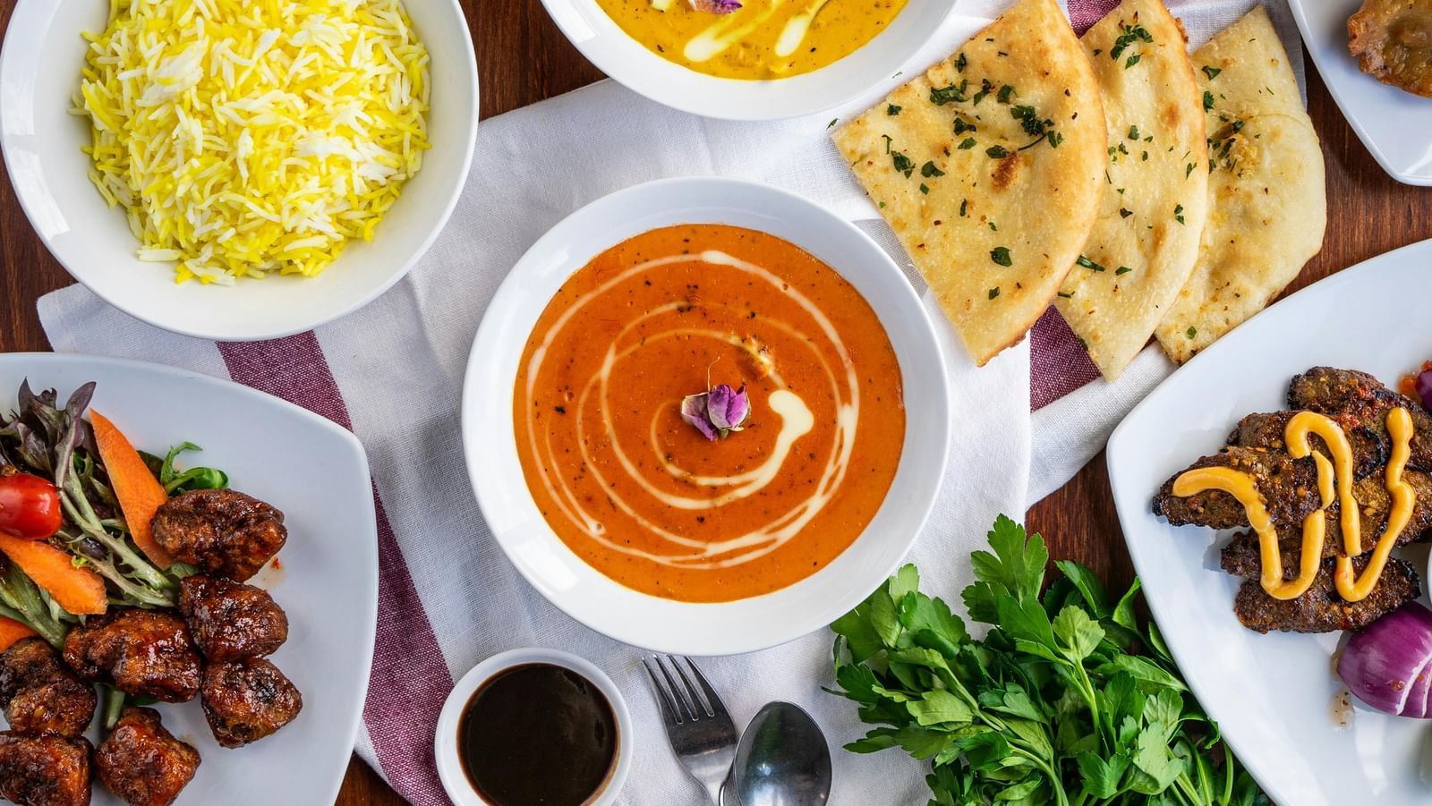 top angle of a wide variety of Indian dishes served on a dining table on white coloured serving dishes