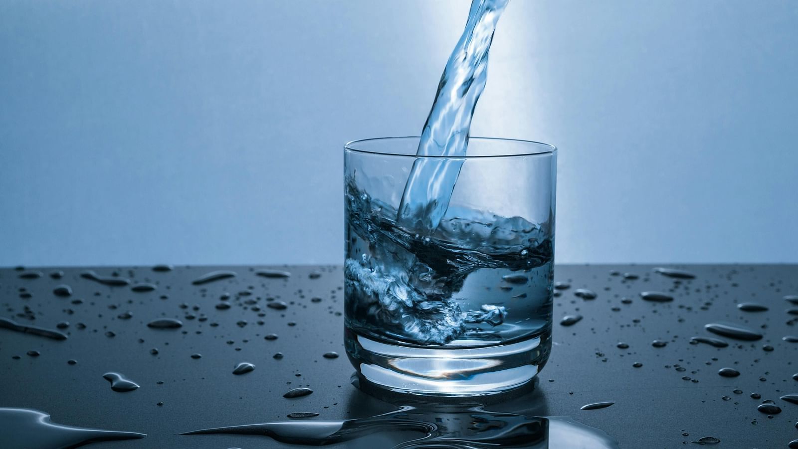 A glass of water being filled, with water splashes around.