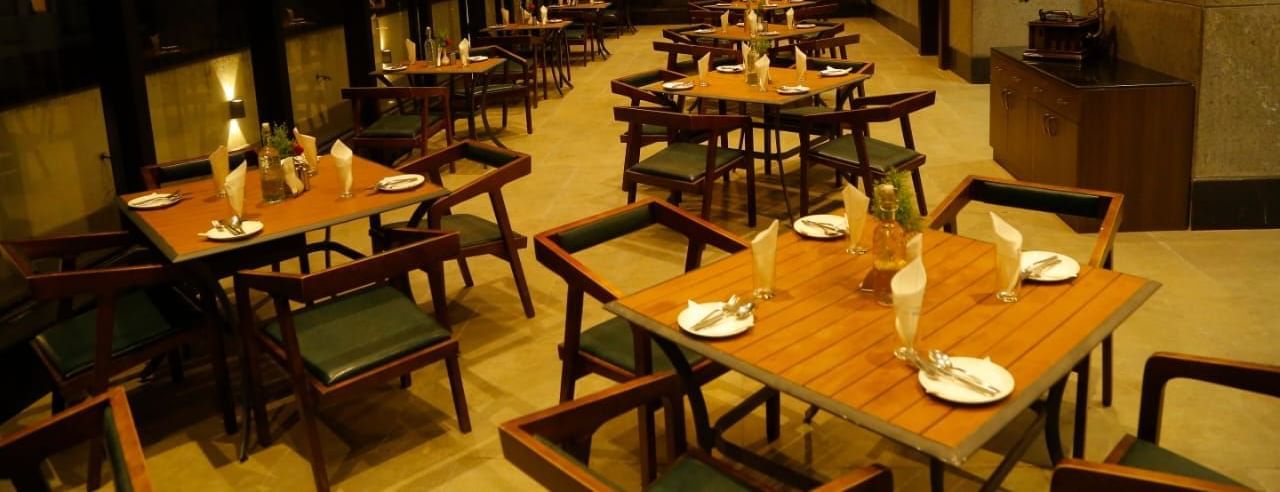 Spacious dining area with tables and chairs set for guests under warm lighting at The Hamuse Hotel, Kodaikanal.