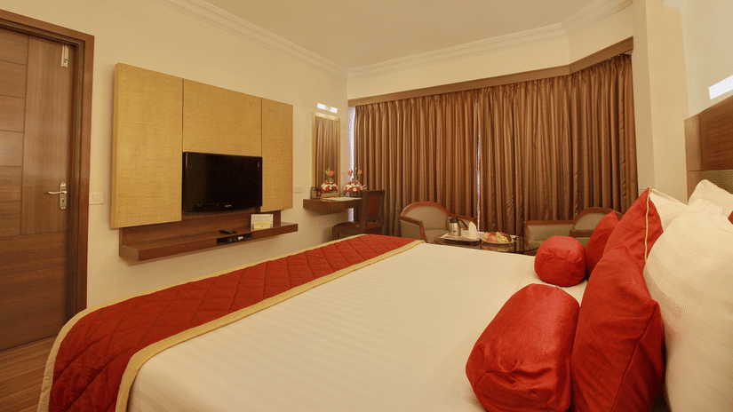 king size bed full view with clean and white linens along with pillows with red cover neatly kept and room amenities like a LED television - The Monarch Hotel, Brigade Road