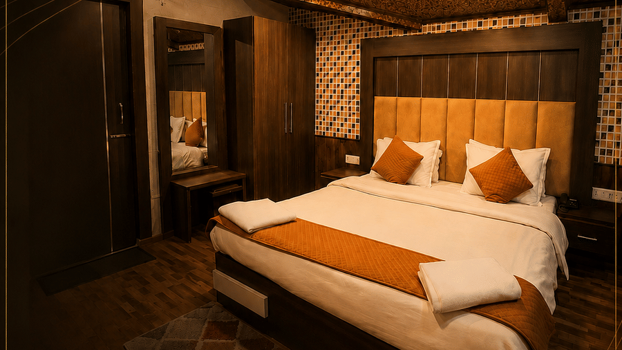 An Executive Room at Hotel Outlook, Pahalgam, featuring a double bed with a tall headboard, a bedside table, a mirror, and patterned flooring.