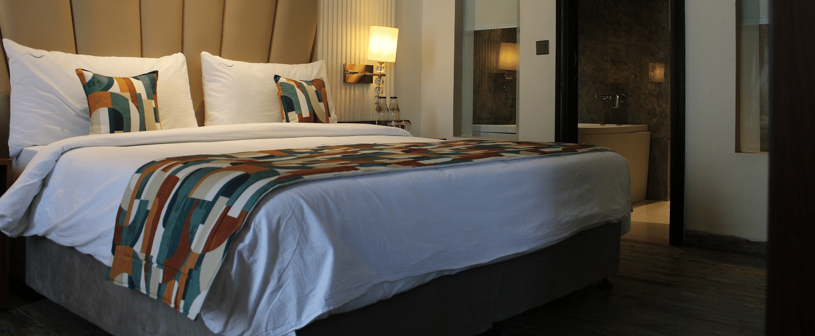 A bedroom with a patterned headboard and a lamp illuminating yellow light next to the bed at BluSalzz Residence, Amritsar.
