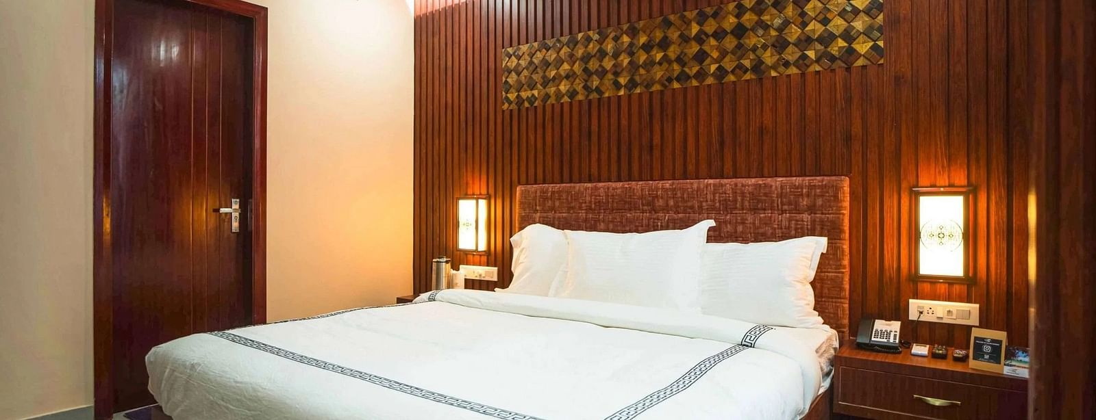 A warmly lit bedroom at Mansha Palace features a plush bed, wooden wall panelling, and bedside tables.