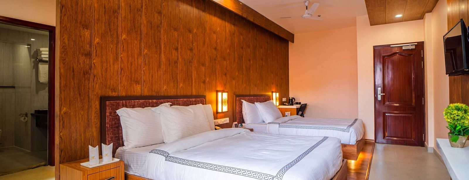 A comfortable hotel room at Mansha Palace features two beds, wooden accents, and a glimpse into the bathroom.