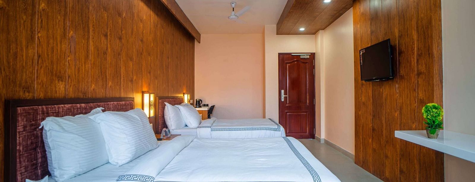 A comfortable hotel room at Mansha Palace features two beds, wooden accents, and a glimpse into the bathroom.