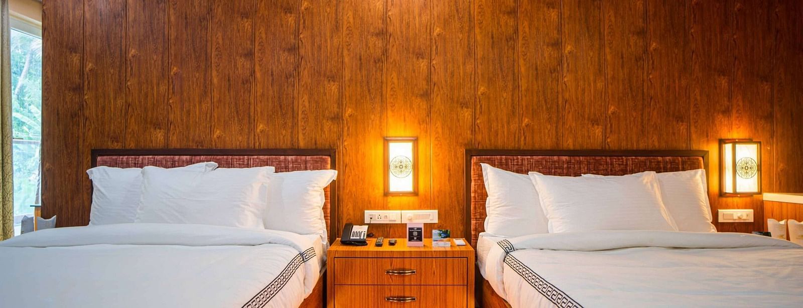 A comfortable hotel room at Mansha Palace features two cozy beds and warm wooden wall paneling.