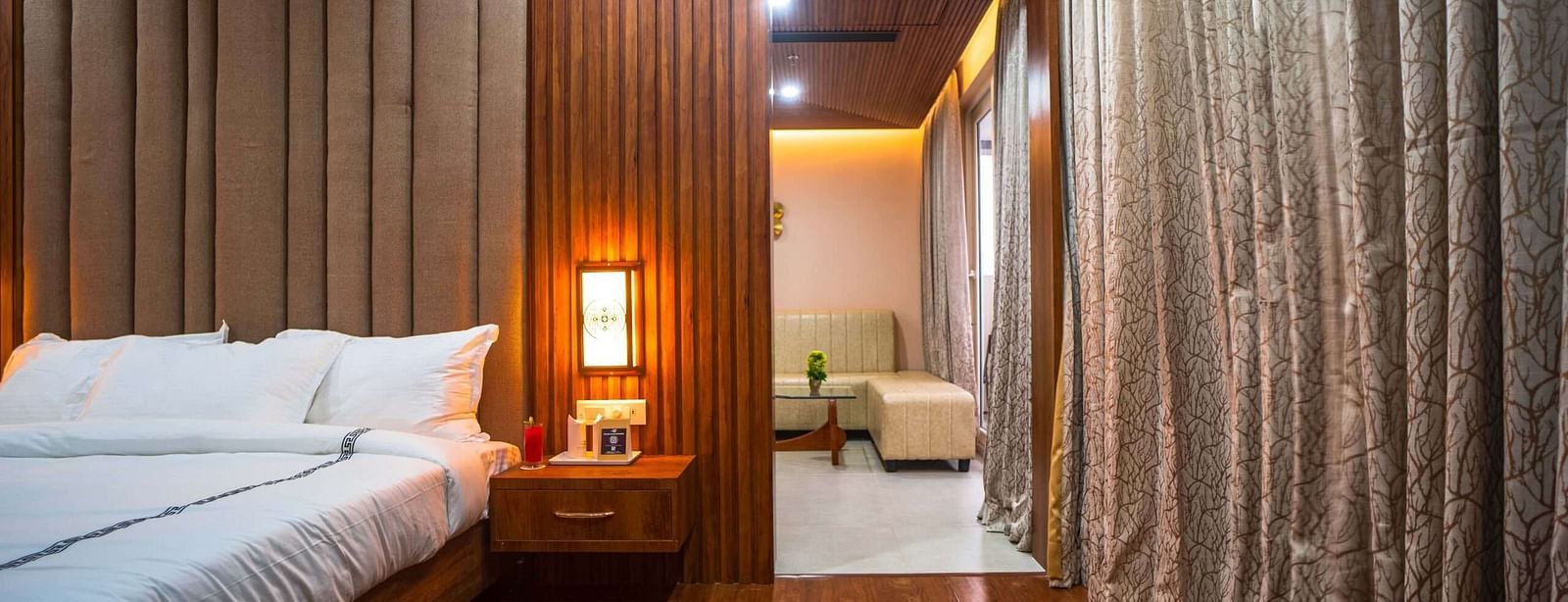 A well-lit bedroom at Mansha Palace features a comfortable bed, wooden accents, and a glimpse into an adjoining seating area.