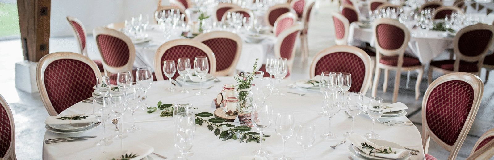 Formal dining setup with round tables, white linens, and red-cushioned chairs for an event.