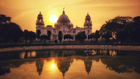 Victoria Memorial in Kolkata at sunset, its marble domes reflected in a pond in the gardens