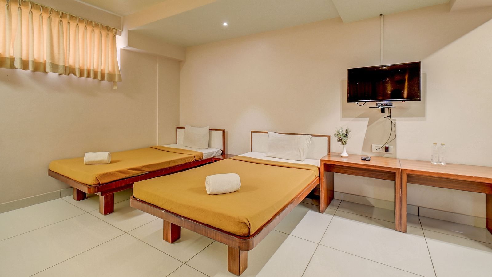 A spacious room at Harigovinda's JNStay, featuring a wall-mounted TV above a wooden table set against the wall, and two beds