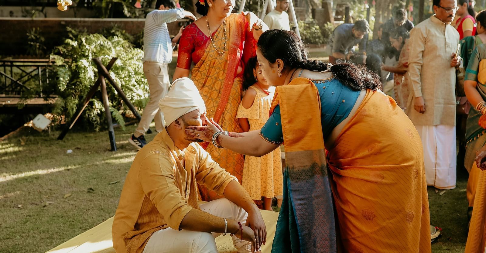 The Indian wedding ritual of haldi being performed in a lawn where a woman is applying turmeric on the groom.