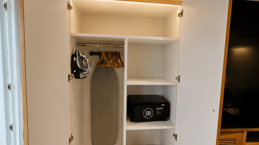 An open wooden wardrobe showing shelves, an ironing board, and a small safe at BluSalzz Collection - Casa Onze, Arpora.