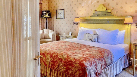 Door opening to the bedroom of Lower Garden Room, revealing it's bed, patterned walls, and a sofa at Tallman Hotel
