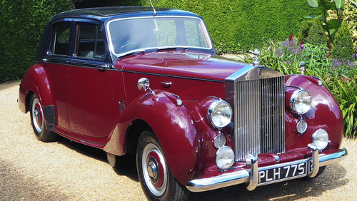 A classic Rolls Royce with sleek silver detailing, elegant curves, and a vintage charm parked in a scenic outdoor setting.