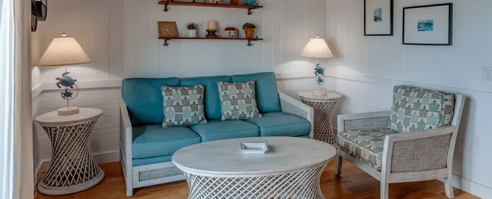 Cozy living room with white wicker furniture, wall-mounted shelves, and wood-style flooring in a seaside cottage | Abaco Inn