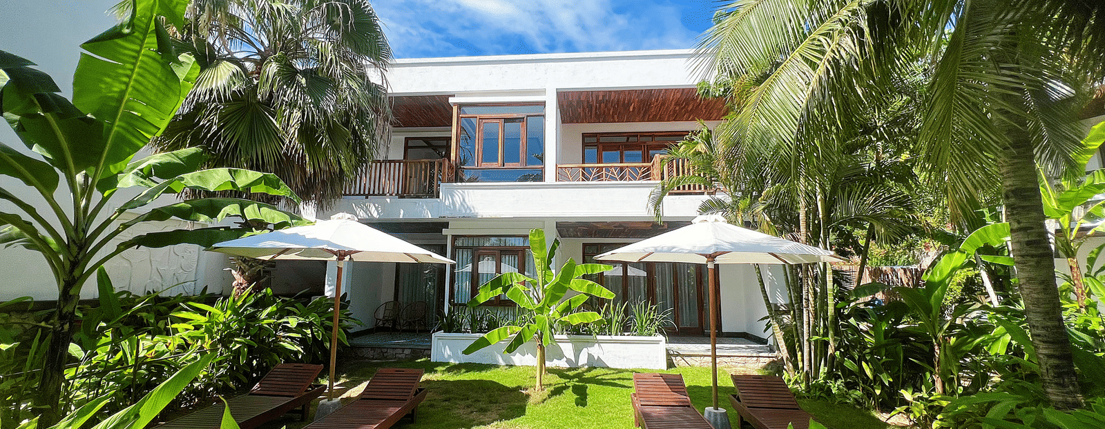 A facade view of Alibu Resort Nha Thrang - A Waterfront Wedding Venue, with trees and a manicured garden in the foreground.