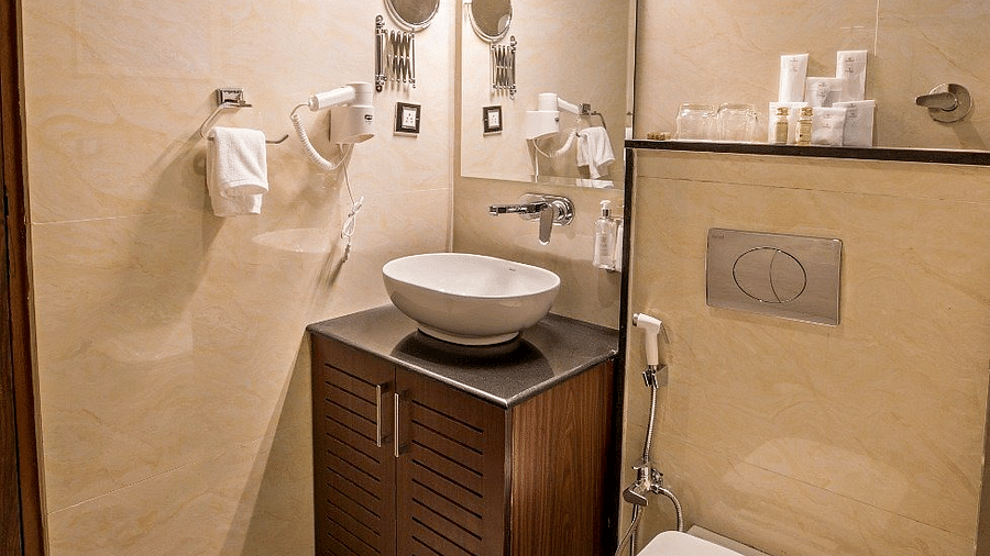 A brightly lit bathroom at Regenta Inn DLS featuring a vanity area along with a commode besides it.