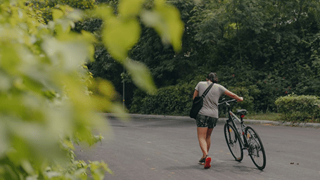 A person holding a cycle and walking on a tarred road - Karma Lakelands.