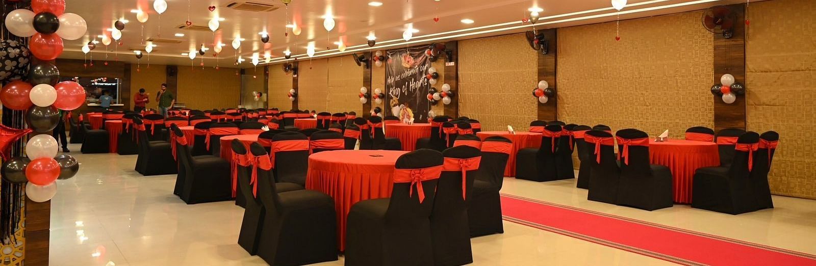Banquet hall with red and black chair covers and ceiling lights at Mansha Regency, Port Blair.