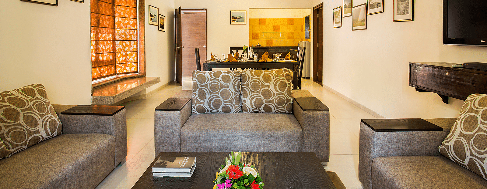 An image of a seating area with photos hanged on the wall, flat TV screen,  and behind the seating area there is a dining table set - The Riverview Retreat, Corbett