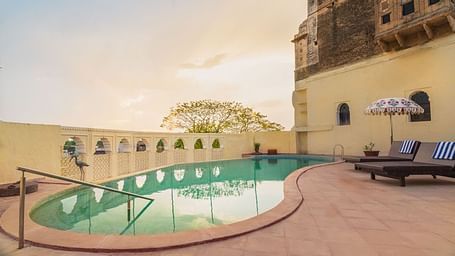 A tranquil pool at Fort Barli, flanked by historic walls and lounge chairs, offers a serene escape with a touch of grandeur.