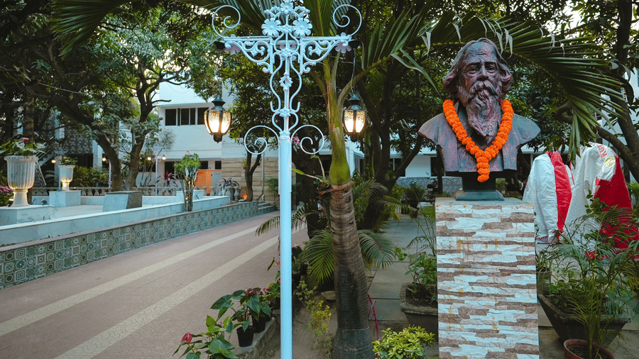 A bronze portrait bust sculpture on a stone pedestal next to an ornate street lamp post along a resort pathway.