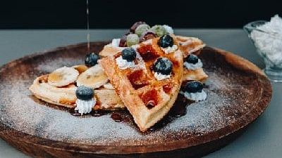 Hand pouring syrup over waffles topped with berries on a wooden plate at Karma Chalets.