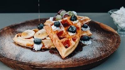 Hand pouring syrup over waffles topped with berries on a wooden plate at Karma Chalets.