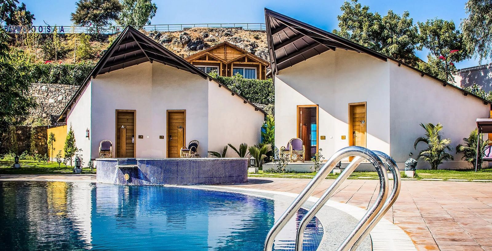 Two modern bungalows with pointed roofs flank a swimming pool.