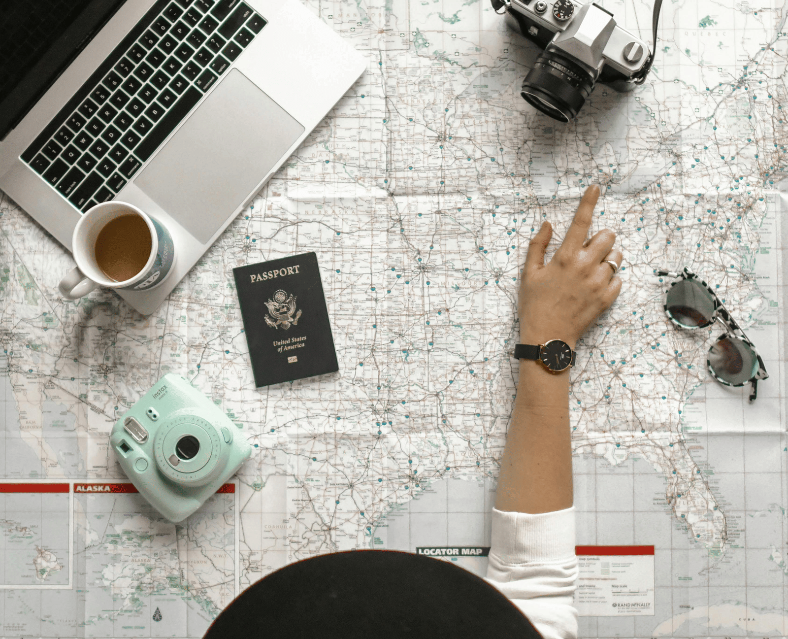 Top view of a workspace with travel essentials, including a laptop, map, camera, and coffee cup.