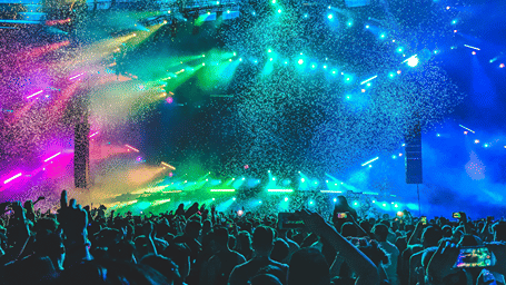 Large crowd enjoying a live music festival with vibrant stage lights, colorful confetti, and an energetic concert atmosphere.