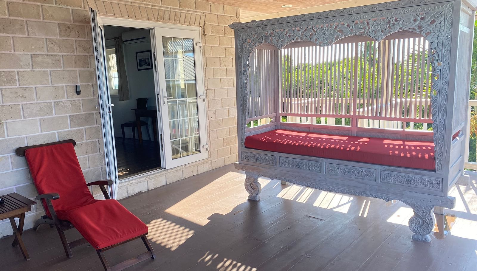 Veranda with red lounge chairs and sunlight streaming through white railing | A Stone's Throw Away