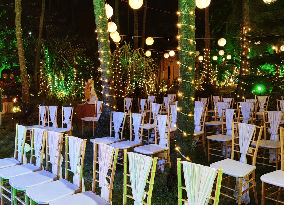 Outdoor wedding seating with white chairs and lights arranged among palm trees at Paradise Lagoon Resort, Udupi.