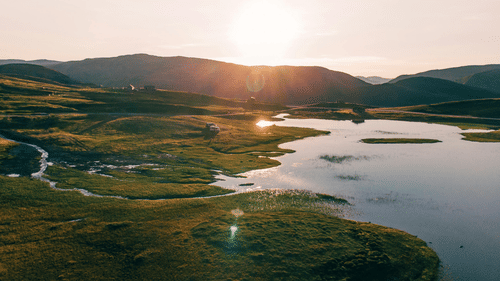 An image of a plateau with a lake surrounded by greenery and beautiful sun rays hitting the mountains in the background