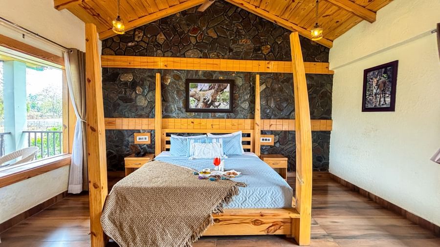 Elegant bedroom with four-poster bed and rustic decor at Corbett Nirvana Resort.