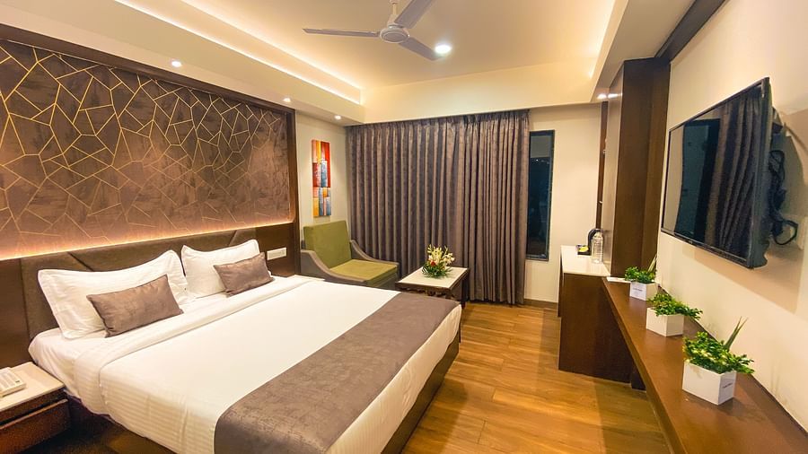 a bedroom with a large bed facing a mounted television and a green chair in the corner - Jardin Hotels, Indore