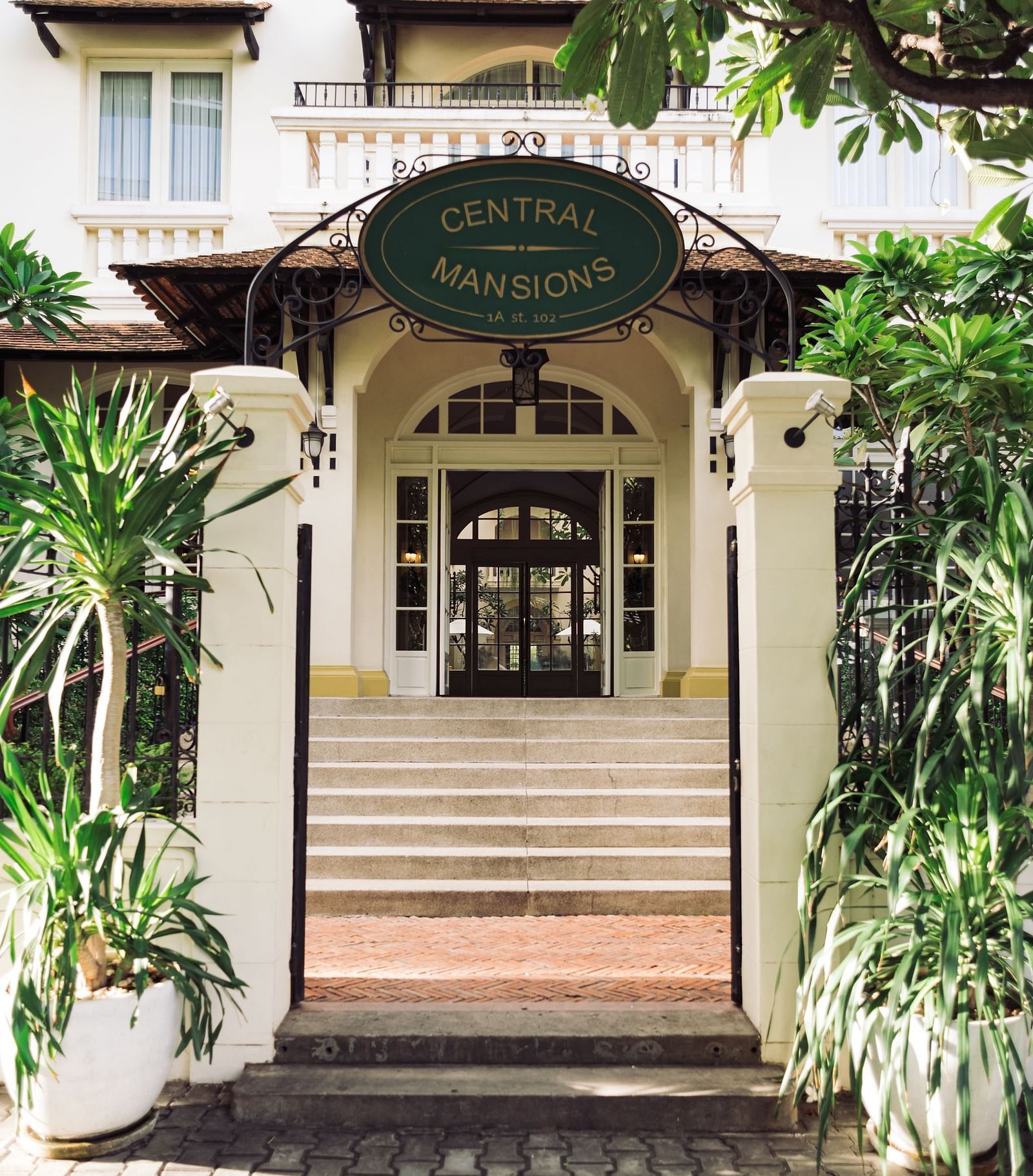 A narrow view of an ornate entrance with a staircase and greenery | Central Mansions, Phnom Penh