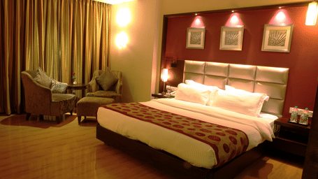 A warmly lit deluxe room of Lords Plaza Surat featuring a king size bed, comfortable seating and modern interiors