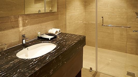 A bathroom with a glass shower enclosure, sink, mirror, and towel rack at The Hamuse Hotel, Kodaikanal.