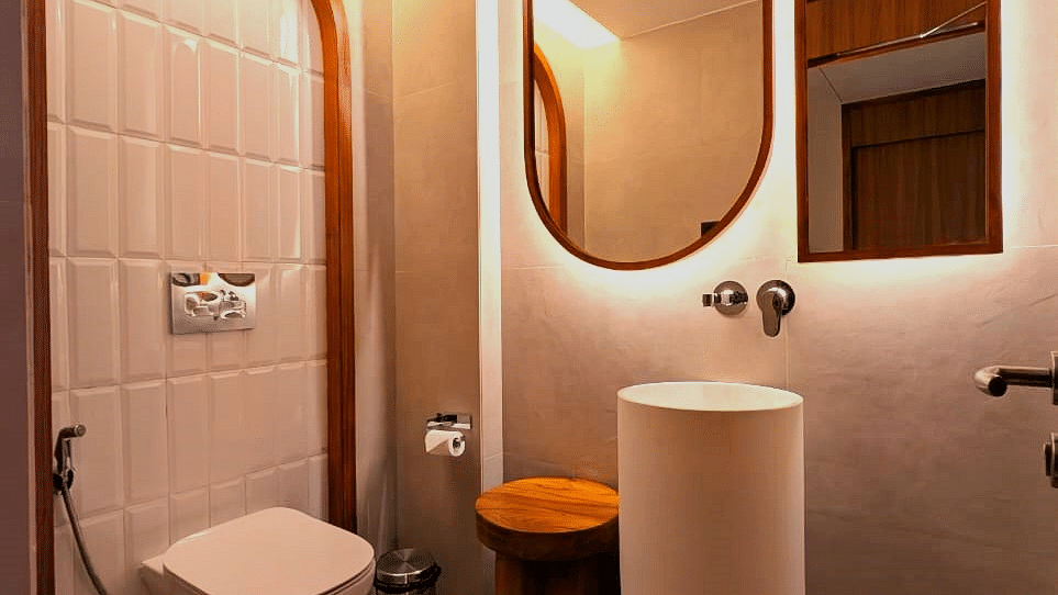  A modern bathroom at Swosti Premium Beach Resorts, Puri, with a powder room, sink, and unique mirror design.