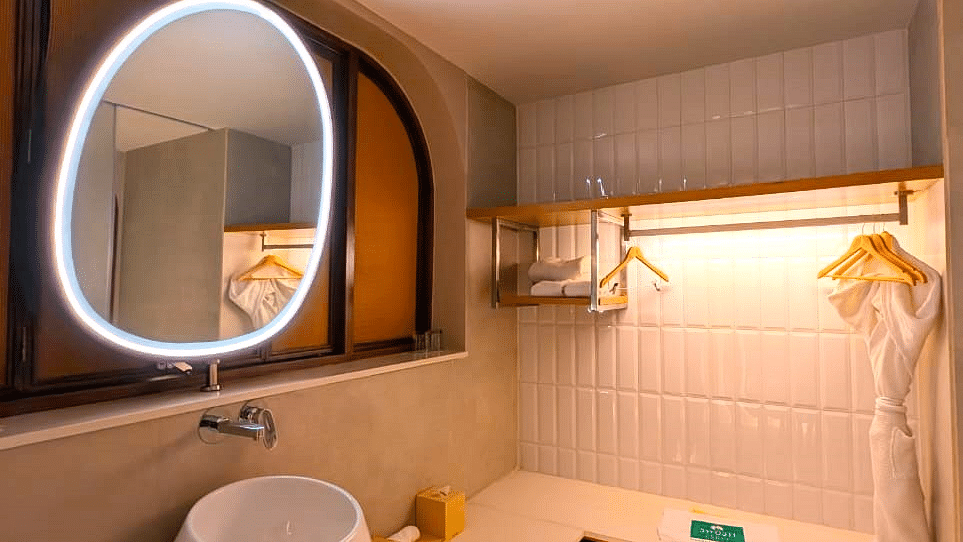 A bathroom at Swosti Premium Beach Resorts, Puri, with a unique oval mirror and a sink.