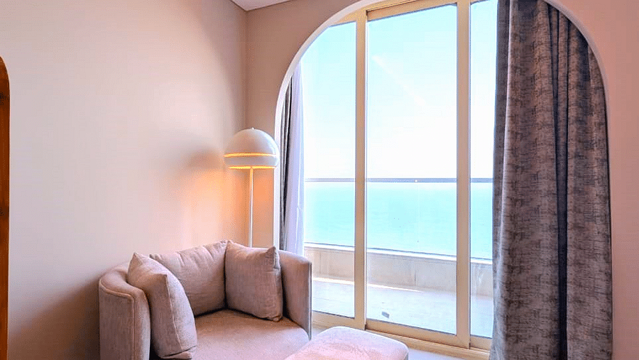 A partial view of a living area at Swosti Premium Beach Resorts, Puri, with a chair and an arched window.