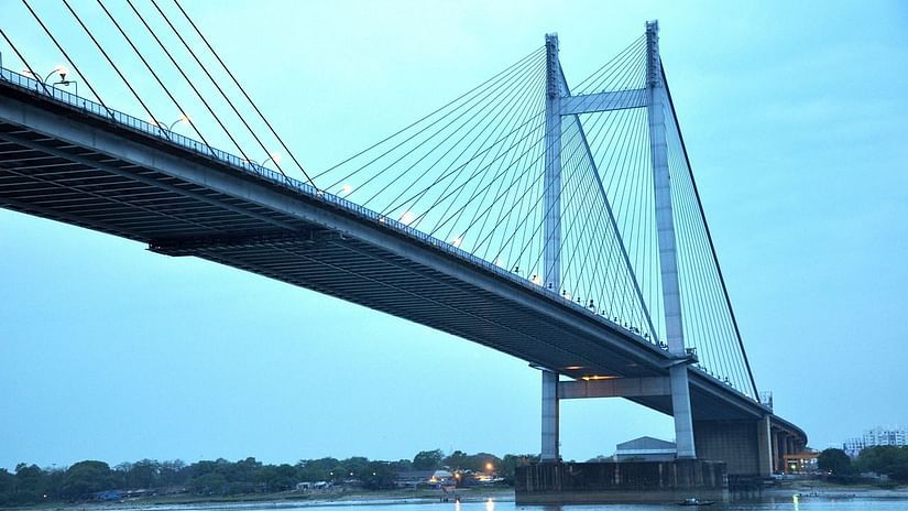 Large suspension bridge spanning over a calm river with boats underneath at twilight.