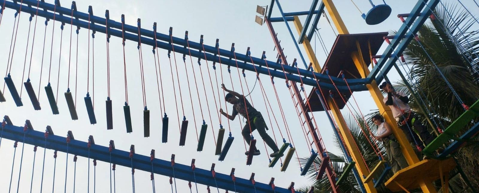 Silhouetted figures climb an outdoor adventure course structure with ropes and ladders