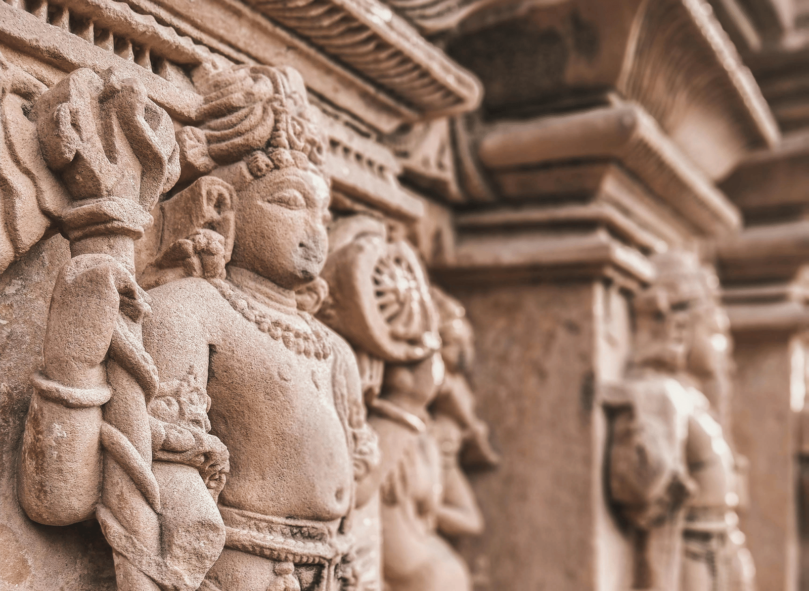 Ornate sandstone carvings of standing Hindu deities lining a temple wall.